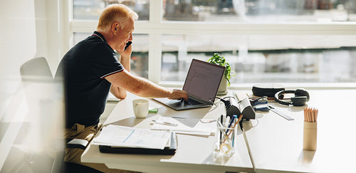 Businessman talking over phone while working on laptop