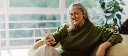 Senior woman checks a smartphone beside a houseplant
