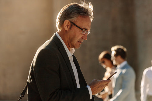 Senior man using mobile phone while walking on street to office