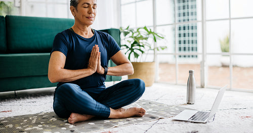 Meditating in a yoga class at home, mature woman sitting in prayer pose