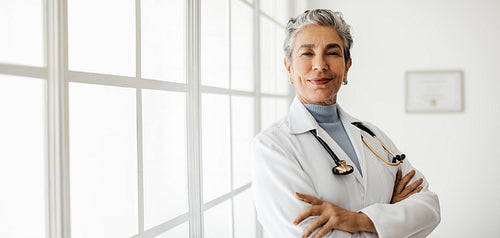 Senior doctor in a lab coat standing with her arms crossed, inspiring trust and confidence