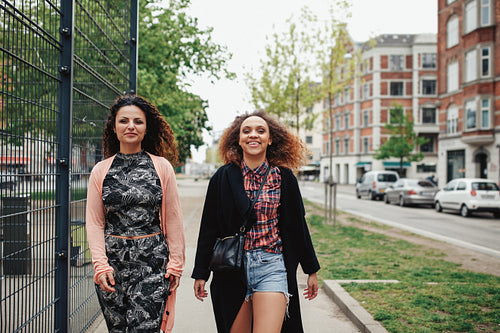 Two girlfriends walking along city street 