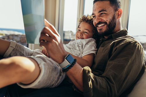 Father and son reading a book sitting on a couch at beach house