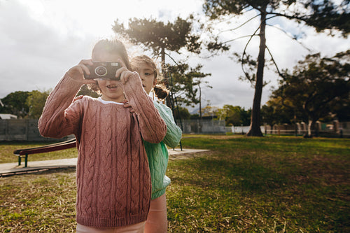 Twin sisters taking pictures with old camera at the playground