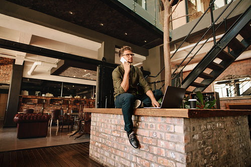 Creative young man with laptop talking on phone