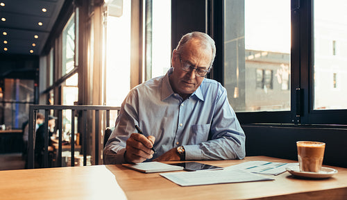 Mature businessman in cafe making notes
