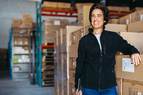 Cheerful warehouse manager standing next to a stack of cardboard boxes