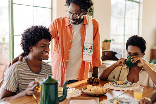 Happy Brazilian dad serving his family with a traditional cheese bread rolls breakfast at home