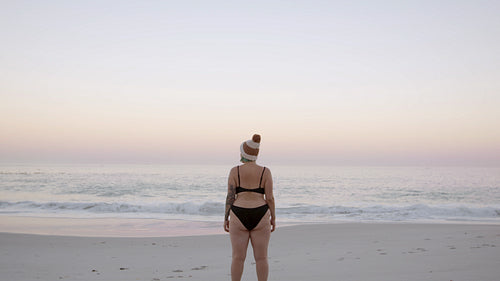 Woman at the beach looking at the sea during sunset