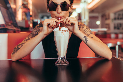 Woman drinking milkshake with a straw sitting at a diner
