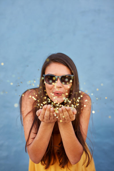 Happy young woman blowing confetti in the air