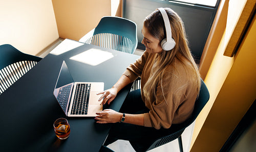 Young woman using a laptop while listening to music in a modern setting