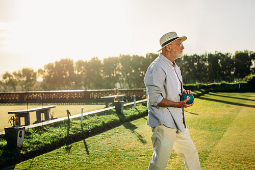 Elderly man standing in a lawn holding a boule