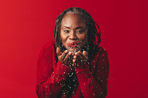 Black woman with dreadlocks blowing confetti in a studio