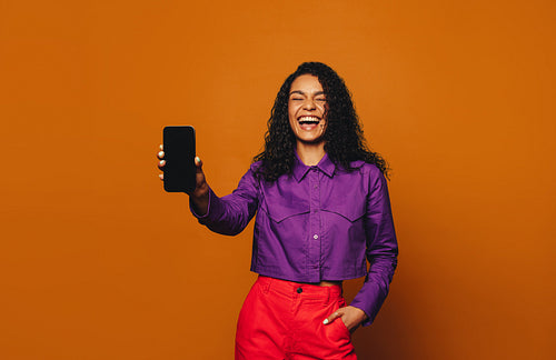 Cheerful woman showing vibrant colour blocking on a orange background with a mobile device