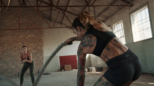 Female athlete doing battle rope exercise with her trainer