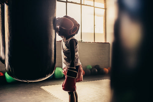Boxing kid standing in front of a punching bag at a boxing gym