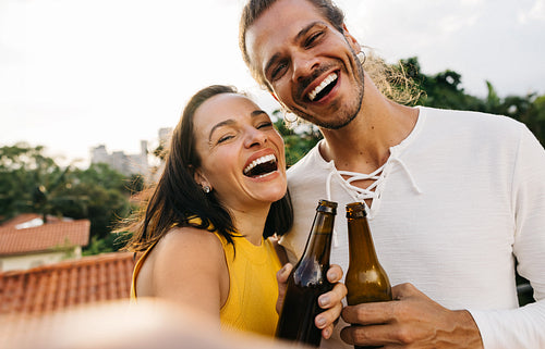Friends taking a selfie with drinks, enjoying beer, and smiling happily outdoors