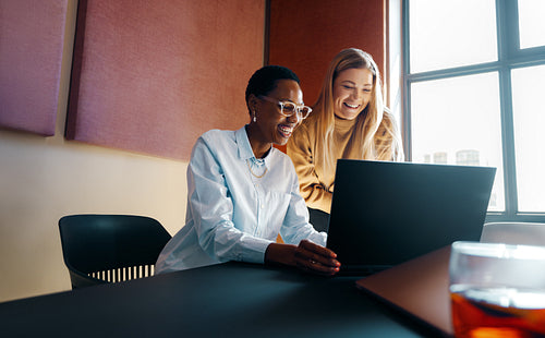Two colleagues smiling and working together at a laptop in a modern office