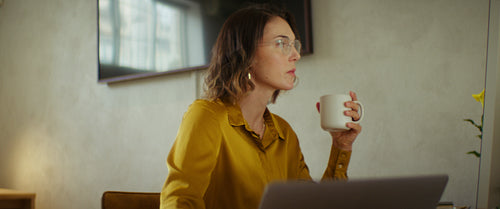 Businesswoman working from home office on laptop while drinking coffee