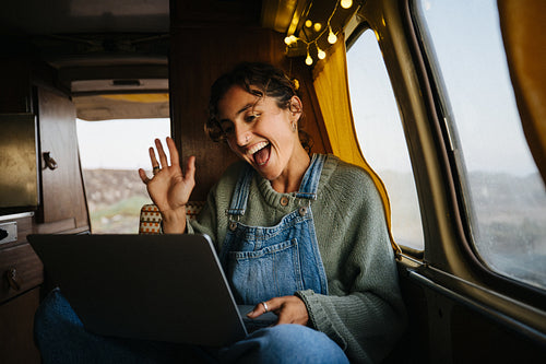 Woman chats and waves while working on a laptop inside a cozy van