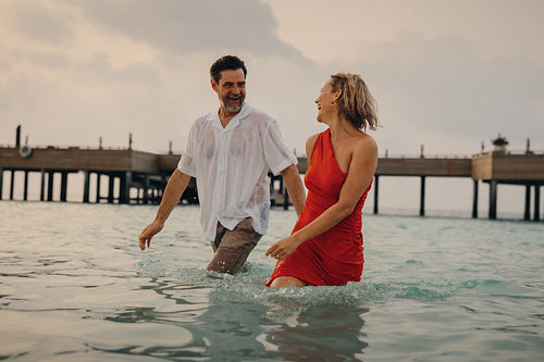Older couple enjoying a luxury beach vacation, walking in the ocean water and laughing happily