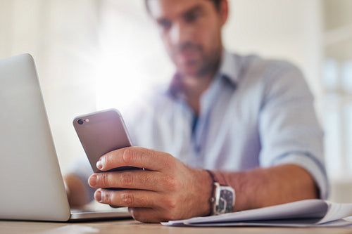 Young man using mobile phone while working on laptop