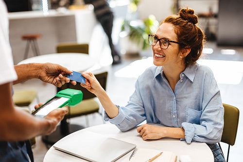 Female customer paying her bill with a credit card in a cafe