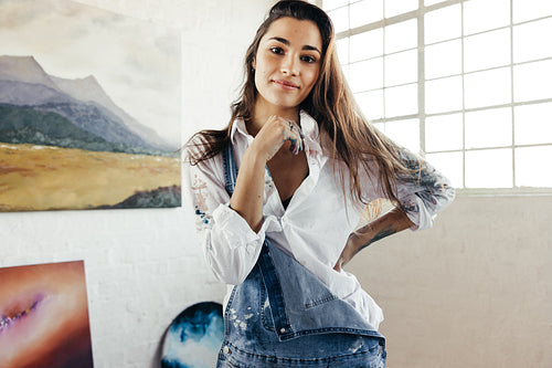 Young female artist standing in front of her paintings