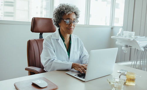 Woman dentist managing digital documentation on a laptop at her clinic desk