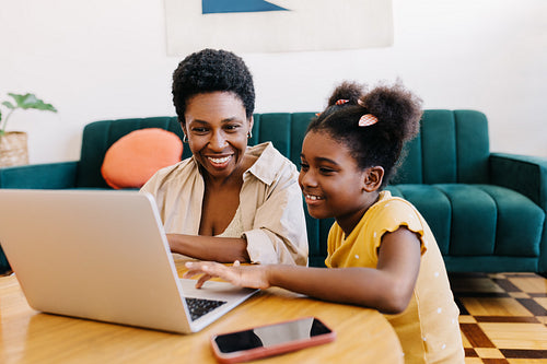 Girl and her mother sitting together at home, selecting a movie on a laptop