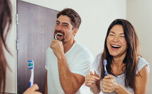 Smiling couple brushing teeth in bathroom