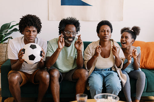 Brazilian family watching a football game with fingers crossed