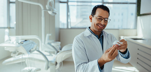 Smiling male dentist holding dental model in modern clinic