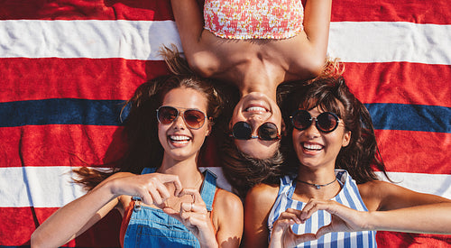 Beautiful friends with heart sign lying at the beach