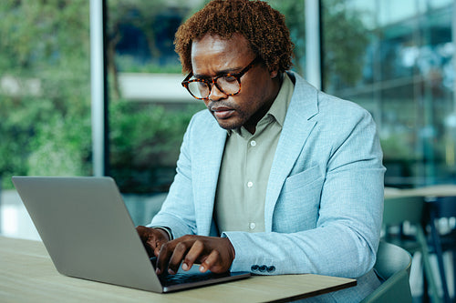 Focused African businessman working on laptop in modern office