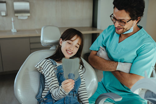 Young patient checks her teeth with mirror after dental exam