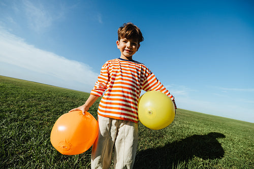 Young boy outdoors with balloons in a sunny field