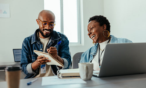 Happy colleagues writing notes and sharing ideas in a collaborative office environment