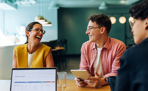 Group of three young coworkers smiling and discussing in a casual office setting