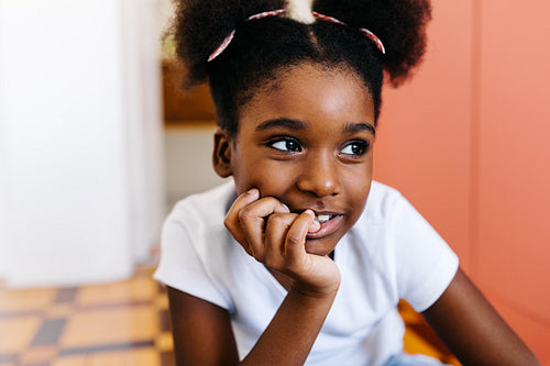 Pensive young girl with afro hair sitting on the floor, looking away and smiling
