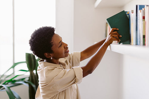Black woman selecting a book from her book collection at home