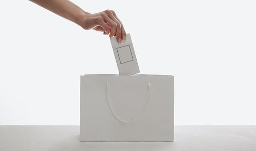 Hand placing perfume box into white shopping bag for retail and gift mockups