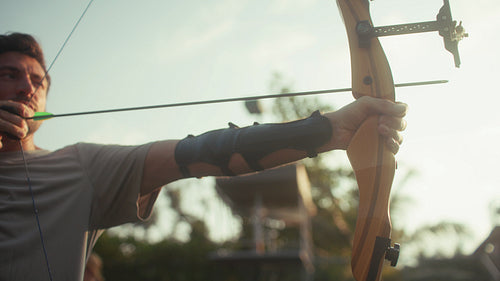 Young man practicing archery and aiming a bow and arrow during golden hour