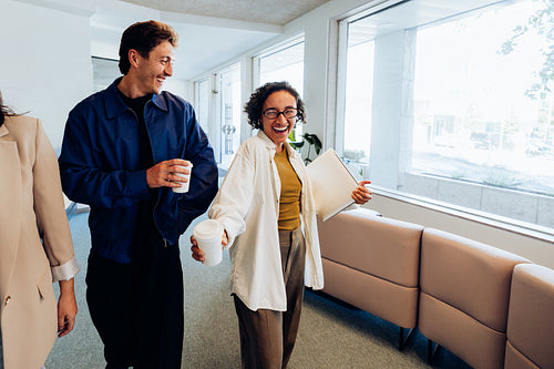 Two colleagues share coffee and smile in an office