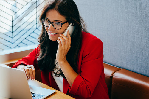 Confident professional woman on a mobile call at a desk with a laptop