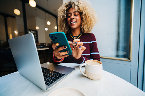 Woman using smartphone and laptop while smiling in cafe