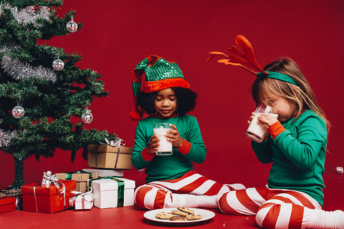 Kids drinking milk sitting beside a christmas tree