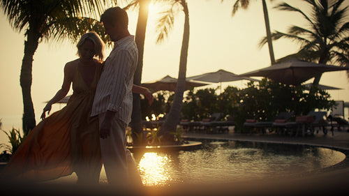 Romantic couple embraces by the tropical pool at golden hour during their luxurious sunset vacation