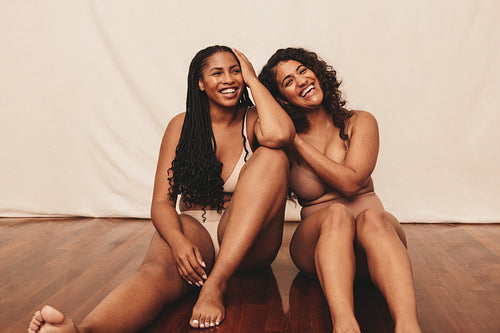 Best friends smiling while sitting in underwear
